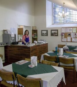 A volunteer stands behind the counter of the cafe with tables set in the foreground